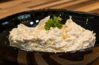 Cheese – Garlic Dip and Spread piled in a black bowl, garnished with parsley, on a wooden table.
