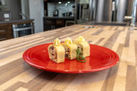 Three slices of Cheese Roulade with Goat Cheese & Raisins on a red plate, each topped with a piped yellow swirl.