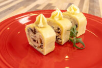 Three sliced pieces of Cheese Roulade with Goat Cheese & Raisins topped with piped goat cheese on a red plate.