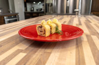 Three sliced rounds of Cheese Roulade with Goat Cheese & Raisins, piped topping, on a red plate.