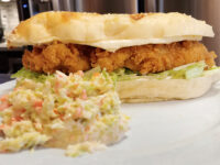 Bowl of creamy Coleslaw with shredded cabbage and carrot, served alongside a fried chicken sandwich.