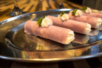 Four Creamy Horseradish Ham Rolls piped with white cream and topped with herb garnish, arranged on a shiny metal platter.