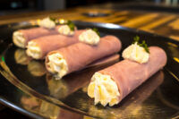 Rolled Creamy Horseradish Ham Rolls piped with white filling, garnished with parsley, on a black plate
