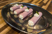 Four Creamy Ham Rolls piped with white filling and garnished with parsley, arranged on an oval metal platter atop a wooden table