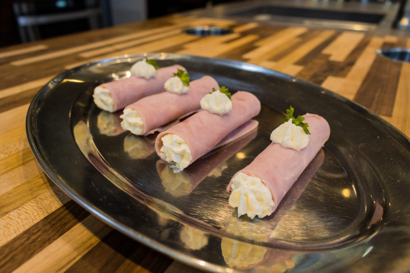 Six Creamy Ham Rolls piped with white cream filling and garnished with parsley, arranged on a round metal plate.