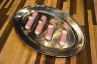 Four Creamy Horseradish Ham Rolls piped with white cream and garnished with herb leaves on a metal tray.