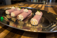 Four Creamy Ham Rolls piped with white filling and topped with herb leaves, arranged on a metal tray.