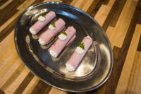 Four Creamy Horseradish Ham Rolls piped with white filling and topped with parsley on a silver platter.