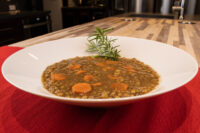 Bowl of Czech Lentil Soup Čočková Polévka with carrot slices, topped with a rosemary sprig.