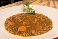 White bowl of Czech Lentil Soup Čočková Polévka with carrot slices and a herb sprig on a wooden table.