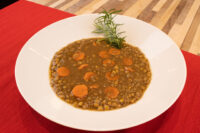 White bowl of Czech Lentil Soup Čočková Polévka with carrot slices, garnished with a rosemary sprig.