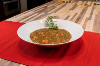 Bowl of Czech Lentil Soup Čočková Polévka with carrot slices, topped with a rosemary sprig, on a red mat.