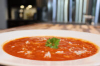 White bowl of Czech Tomato Soup with Rice topped with grated cheese and a parsley leaf.