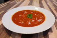 White bowl of Czech Tomato Soup with Rice, garnished with parsley, on a striped wooden table.