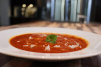 White bowl of Czech Tomato Soup with Rice, garnished with parsley and scattered rice grains.