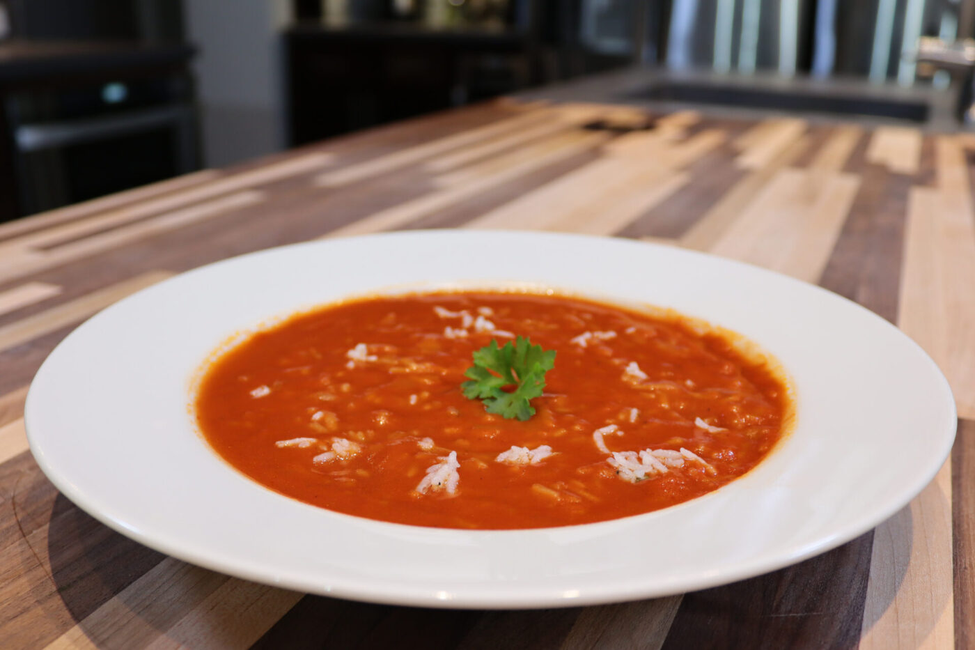 White bowl of Czech Tomato Soup with Rice topped with grated cheese and parsley, on a wood counter.