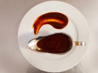 Dark reddish-brown Demi-Glace Sauce (easy version) swirled on a plate beside a filled gravy boat