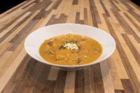 Bowl of Frankfurt Soup Frankfurtská Polévka with meat chunks, sour cream dollop, and chives on a wood table.