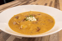 Bowl of Frankfurt Soup Frankfurtská Polévka with orange-yellow broth, chunks, sour cream, and chives.