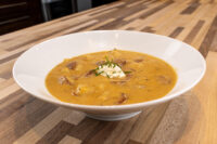 Bowl of Frankfurt Soup Frankfurtská Polévka topped with sour cream and chives on a wooden table.