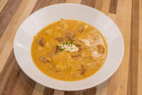 Bowl of Frankfurt Soup Frankfurtská Polévka with potato and sausage chunks, topped with sour cream and chives, on a wooden table.