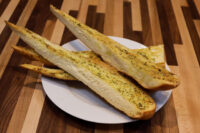 Herb Baguette sliced into long pieces with herb-flecked topping on a white plate.