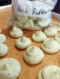 Piped mounds of herb butter on parchment paper with a bag labeled 'Herb Butter' in the background.