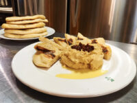 Whipped Hummus drizzled with olive oil and topped with a dark relish, served with grilled flatbread wedges.