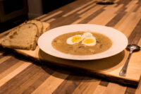 Kulajda Soup White bowl of creamy Kulajda Soup topped with two soft-boiled egg halves, served with bread on a wooden board.