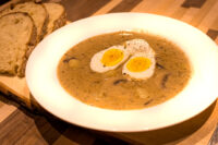 Kulajda Soup Bowl of Kulajda Soup with mushrooms and potatoes, topped with a halved soft-boiled egg, served with bread.