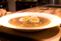 Kulajda Soup White bowl of creamy Kulajda Soup topped with two egg halves and black pepper, bread beside it.