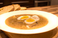 Kulajda Soup White bowl of Kulajda Soup with mushroom pieces, dill, and soft-boiled egg halves, sliced bread behind.