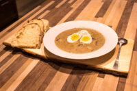 Kulajda Soup Bowl of Kulajda Soup topped with halved soft-boiled eggs, served with crusty bread on a wooden board.