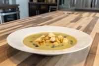 Leek Soup White bowl of creamy pale green Leek Soup topped with crispy croutons and herbs on a wooden counter.