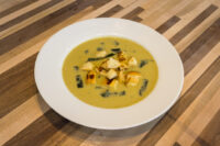 Leek Soup Bowl of pale green Leek Soup topped with crispy croutons and thin leek strips on a striped wooden table.