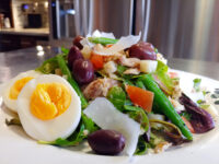 Plated Niçoise Salad with Tuna showing halved eggs, olives, green beans, tomato, and shaved parmesan