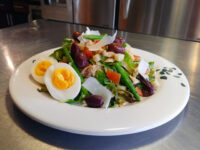 Niçoise Salad with Tuna on a white plate with green beans, olives, tomato, cheese shavings, and a halved egg.