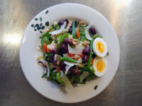Niçoise Salad with Tuna on a white plate with egg, green beans, kalamata olives and shaved cheese.