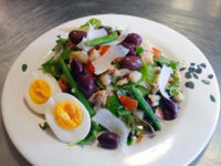 Niçoise Salad with Tuna on a leaf-patterned plate with green beans, olives, egg halves, and shaved cheese.