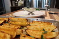 Crispy Oven-Roasted Potato Wedges topped with chives on a metal tray, gravy boat blurred behind.