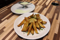 Crispy Oven-Roasted Potato Wedges topped with chives, served beside a gravy boat of pale green dip.