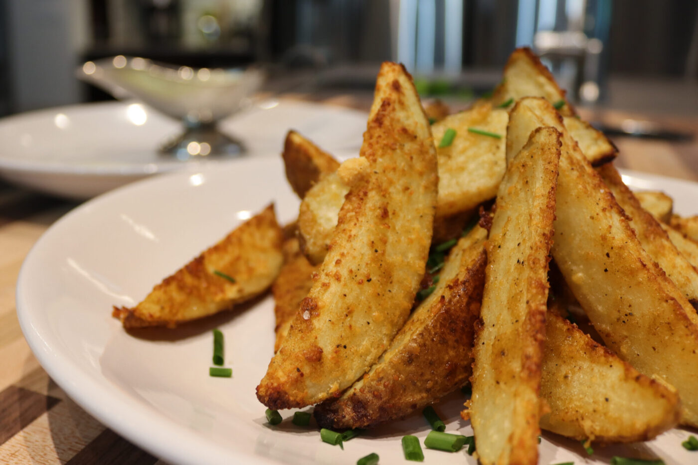 Crispy golden Oven-Roasted Potato Wedges piled on a white plate, topped with chopped chives.