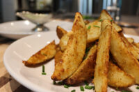 Crispy golden Oven-Roasted Potato Wedges piled on a white plate, topped with chopped chives.