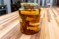 Jar of Pickled Brie Cheese Nakladany Hermelin wedges layered with onion strands and herbs in oil.