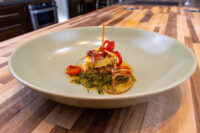 Pickled Brie Cheese Nakladany Hermelin wedge in oil with onion rings, red chili, and rosemary in a ceramic bowl.
