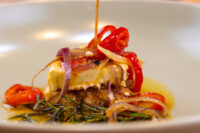 Close-up of nakládaný hermelín, oil running down the skewer over marinated brie, pepper and onion.