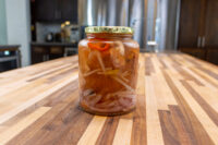 Jar of Pickled Sausage Utopenec with onion slices, chili strips, and orange chunks in vinegar brine.