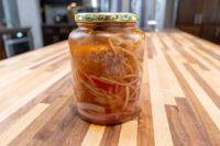 Glass jar of Pickled Sausage Utopenec with sausage, onions, and red pepper in brine on a wood counter.