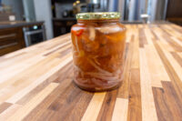A glass jar of Pickled Sausage Utopenec with sausage chunks, onions, and chili in vinegar sauce, lid on.