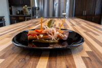 Skewered pickled sausage pieces with onion and pepper strips, Pickled Sausage Utopenec on a black plate.